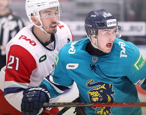 Хоккейный матч. Игрок в бело-красной форме борется за шайбу с игроком в бирюзовой форме. На форме игроков видны логотипы и номера. Сцена на ледовой арене, в движении